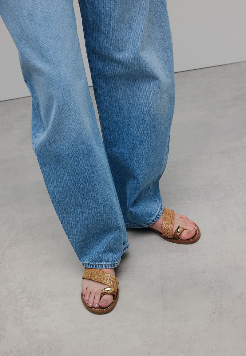 Light wash denim wide-leg jeans, paired with brown woven sandals featuring a gold accent. Smooth texture and relaxed fit.