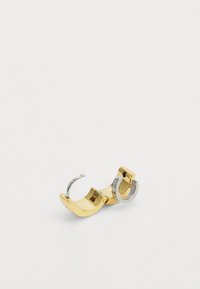 Anello in metallo d'oro e argento con un design curvo e scultoreo. Presenta superfici lisce e una combinazione di finiture lucide e opache.