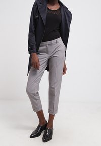 Gray tailored trousers with a slim fit and cuffed hems, paired with a black lace tank top and a navy trench coat, completed with black loafers.