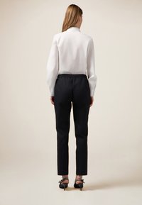 Camicia bianca a maniche lunghe con colletto dritto abbinata a pantaloni neri affusolati con cintura elastica. Scarpe nere con tacco e fiocchi.