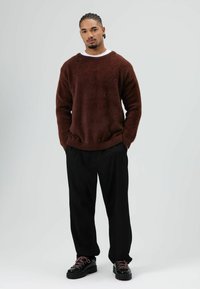 Bruine, zachte trui met een relaxte pasvorm, gecombineerd met zwarte, losse broek en grove zwarte schoenen met roze veters.