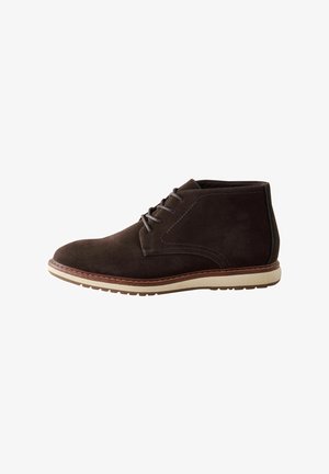 Bottines en suède marron avec une texture lisse, un empiècement arrondi et des lacets. Semelle en caoutchouc beige clair avec un motif de semelle subtil.