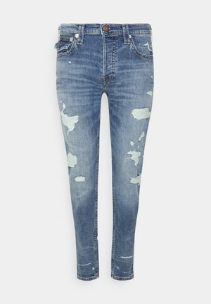 Vaqueros pitillo azules con parches desgastados y descoloridos, con cierre frontal de botón y cremallera, presillas para cinturón y diseño de cinco bolsillos.