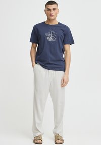 Navyblå bomuld T-shirt med et grafisk design, der viser en sejladsbåd og tekst. Match med lyse, løstsiddende hørbukser og sandaler.