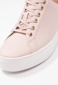 Sneaker in pelle rosa chiaro con lacci piatti, occhielli dorati e suola in gomma bianca. La parte anteriore è arrotondata con dettagli di cuciture sottili.
