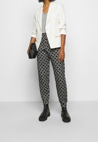 Vit kavaj över en grå topp, i kombination med svarta mönstrade byxor och svarta kraftiga stövlar, håller en svart clutchväska.