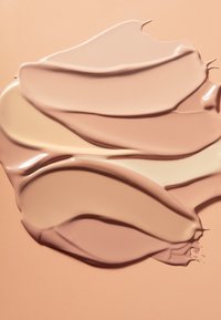 Différentes nuances de fond de teint liquide tourbillonnant harmonieusement sur une surface beige.