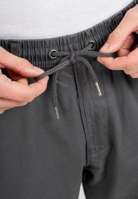 Pantalones cortos grises con cordón ajustable y una cinturilla elástica, que presentan ojales de metal y cordones trenzados con extremos de metal plateado.