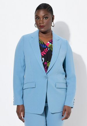 Blazer ajustado de color azul claro con dos bolsillos frontales y cierre de botón, llevado sobre una blusa de patrón floral colorido. Tejido suave y estructurado.