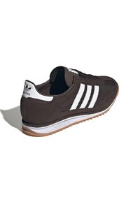 Dark brown suede sneaker with white three-stripe design, textured tongue, and rubber outsole. Rear features logo and smooth leather accents.