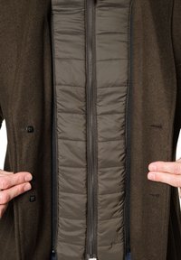 Brązowa kurtka zewnętrzna z pikowaną ciemnoszarym podszewką, z pionowym zamkiem błyskawicznym i guzikami na zewnętrznej warstwie.