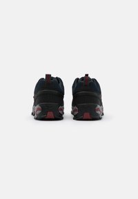 Baskets de sport bleu foncé avec une tige en maille texturée, des accents rouges et une semelle noire robuste. Comprend un col rembourré et des détails réfléchissants.