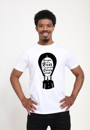 Witte katoenen T-shirt met een zwart bedrukt ontwerp en tekst: "Iedereen is een Freak als je maar goed genoeg kijkt" en een grafische afbeelding van een pak silhouet.