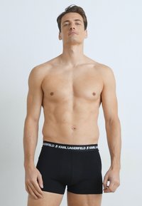 Zwarte boxershorts met een gebrandmerkte tailleband. Gemaakt van een soepele stof. Het model staat rechtop en toont de pasvorm en het ontwerp.