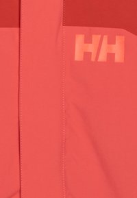 Rote und korallenfarbene Skijacke mit kontrastierenden Paneelen, glatter Textur und reflektierendem "HH"-Logo. Mit Steppnähten entlang der Nähte.