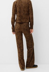 Sada domácího oblečení s leopardím vzorem v hnědých tónech. Elastická tkanina, dlouhé rukávy, volný střih, rozšířené kalhoty, hladká textura, ploché švy.