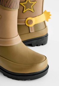Bottes de pluie en caoutchouc brunes avec des accents jaunes, présentant un design d'étoiles, une semelle contrastante et des coutures blanches sur la sangle de cheville.