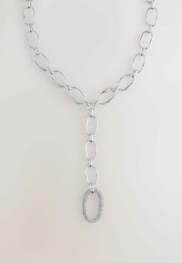 Silberne Kettenneklace mit länglichen ovalen Gliedern und einem herabhängenden ovalen Anhänger, der mit kleinen klaren Steinen auf einem hellen Hintergrund besetzt ist.