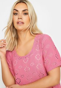 Top rosa con mangas cortas, que presenta un diseño de ojetes florales y recortes circulares. Textura suave y escote redondeado.