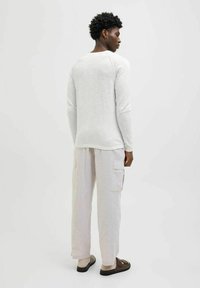Camicia grigia chiara a maniche lunghe con orlo arrotondato, abbinata a pantaloni cargo beige chiaro con tasche laterali. Design semplice, tessuto morbido.