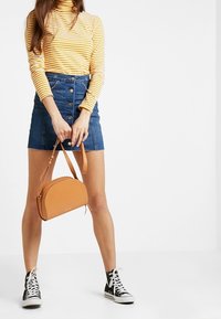 Gul- och vitrandig polotröja, jeansminikjol med knappar framtill, beige läderaxelväska, svarta högklackade sneakers.