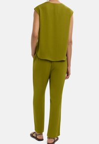 Zestaw oliwkowo-zielony z dopasowaną bluzką i spodniami. Bluzka ma luźny krój i bezrękawnik. Spodnie mają prostą nogawkę i komfortowy fason.