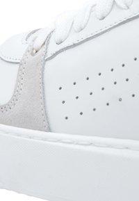 Sneaker bianco con materiali in pelle e camoscio, forma arrotondata, design perforato, lacci piatti e suola in gomma testurizzata.