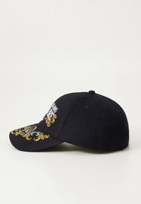 Black baseball cap with a curved brim, featuring yellow and white embroidery of ornate patterns and text on the front. Classic design.