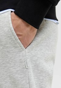 Lichtgrijze fleece joggers met een zijzak, voorzien van een zwarte tailleband en een klein merklabel aan de zaknaad. Zachte textuur.