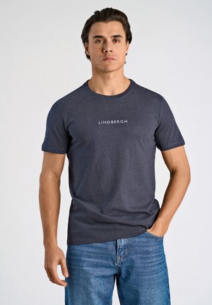 Grå bomulds t-shirt med rund hals og korte ærmer, der har "LINDBERGH" trykt i hvidt over brystet, parret med blå jeans.