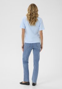 Camiseta de algodón de color azul claro con mangas cortas y un corte relajado, combinada con jeans de denim azul claro y zapatos planos negros, vista desde la parte de atrás.