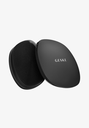 Twee zwarte siliconen gezichtsreinigingspads, één met zachte borstelharen en de ander met het merk "GESKE" op een glad oppervlak.
