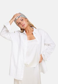 Hvit lin skjorte med lange ermer og knappe-lukking, lagdelt over en hvit cami, kombinert med et mønstrete svart og hvitt hodebånd.