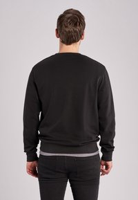Felpa nera con colletto rotondo e maniche lunghe. Presenta un orlo e polsini a costine. Il materiale appare liscio con una finitura uniforme.