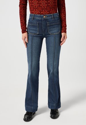 Jeans svasati blu scuro con tasche anteriori e posteriori, cuciture a contrasto e vita alta. Il materiale sembra denim con una texture liscia.