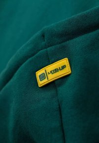 Tessuto verde con una trama morbida presenta un'etichetta rettangolare gialla che mostra "LEVEL UP" in testo blu scuro.