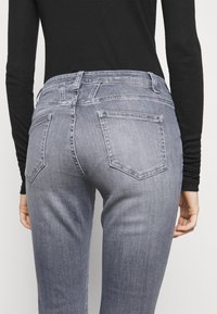 Šedé džíny z denimu s úzkým střihem, mají pět standardních kapes, viditelné švy a pas ve střední výšce.