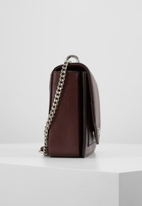Bordeaux læder håndtaske med en struktureret overflade, sølv kædetræk og en elegant, rektangulær form. Frontklap med metalbeslag.