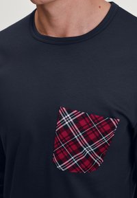 Marineblauw long-sleeve T-shirt met een vierkant rood- en zwart-gecheckt zakje op de linker borst. Glad textuur met een ronde hals.