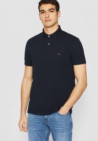 Dunkelblaues Poloshirt mit klassischem Kragen, zwei Knöpfen und kleinem Logo auf der Brust. Aus Baumwollstoff, mit kurzen Ärmeln und taillierter Passform.
