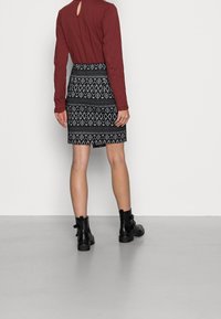 Bourgognefarvet bluse med lange ærmer og nøglehul i ryggen, kombineret med et sort mønstret skørt med geometriske motiver. Bærtes med sorte ankelstøvler.