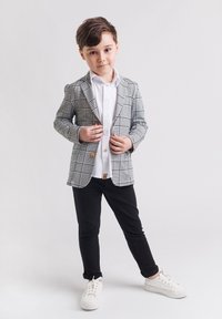 Szary i biały marynarka w kratę z drewnianymi guzikami, biała koszula, czarne spodnie i białe trampki. Gładka faktura i dopasowany krój.