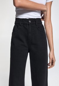 Svarta byxor med avslappnad passform, med ett elastiskt midjeband, två framfickor och en mjuk denimtextur.