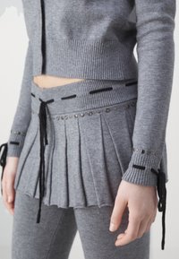 Szary dzianinowy sweter z prążkowanym dołem, spódnica z paskiem i plisami, czarne akcenty oraz metalowe ćwieki. Pasujące dopasowane spodnie dopełniają całość.