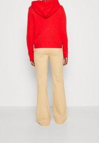 Sweat à capuche rouge court avec capuche et cordon de serrage, associé à un pantalon flare beige avec une texture lisse et des poches arrière.