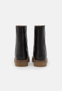 Czarne skórzane botki za kostkę z zamkiem z tyłu, charakteryzujące się brązową gumową podeszwą i gładką fakturą.