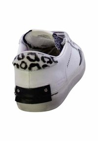 Zapatilla blanca con acentos de estampado de leopardo en el talón, panel de goma negra en la parte trasera y forro de tela texturizada. Detalles de costura únicos visibles.