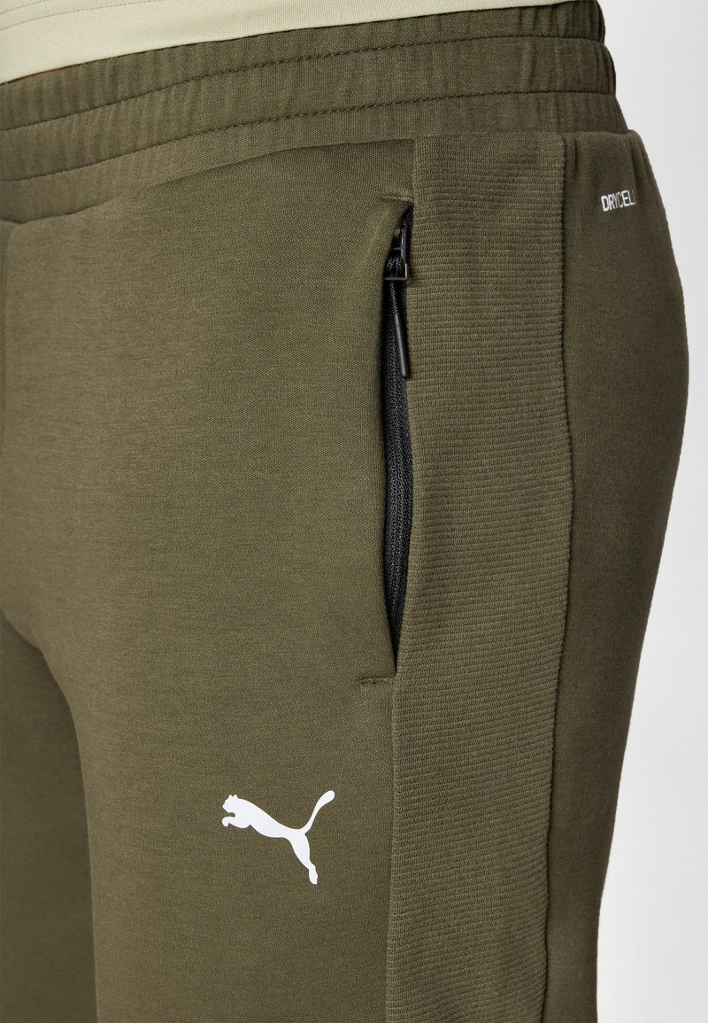 Pantalons de survêtement vert olive en tissu doux, dotés d'une poche zippée noire et d'un logo Puma blanc sur le côté gauche.