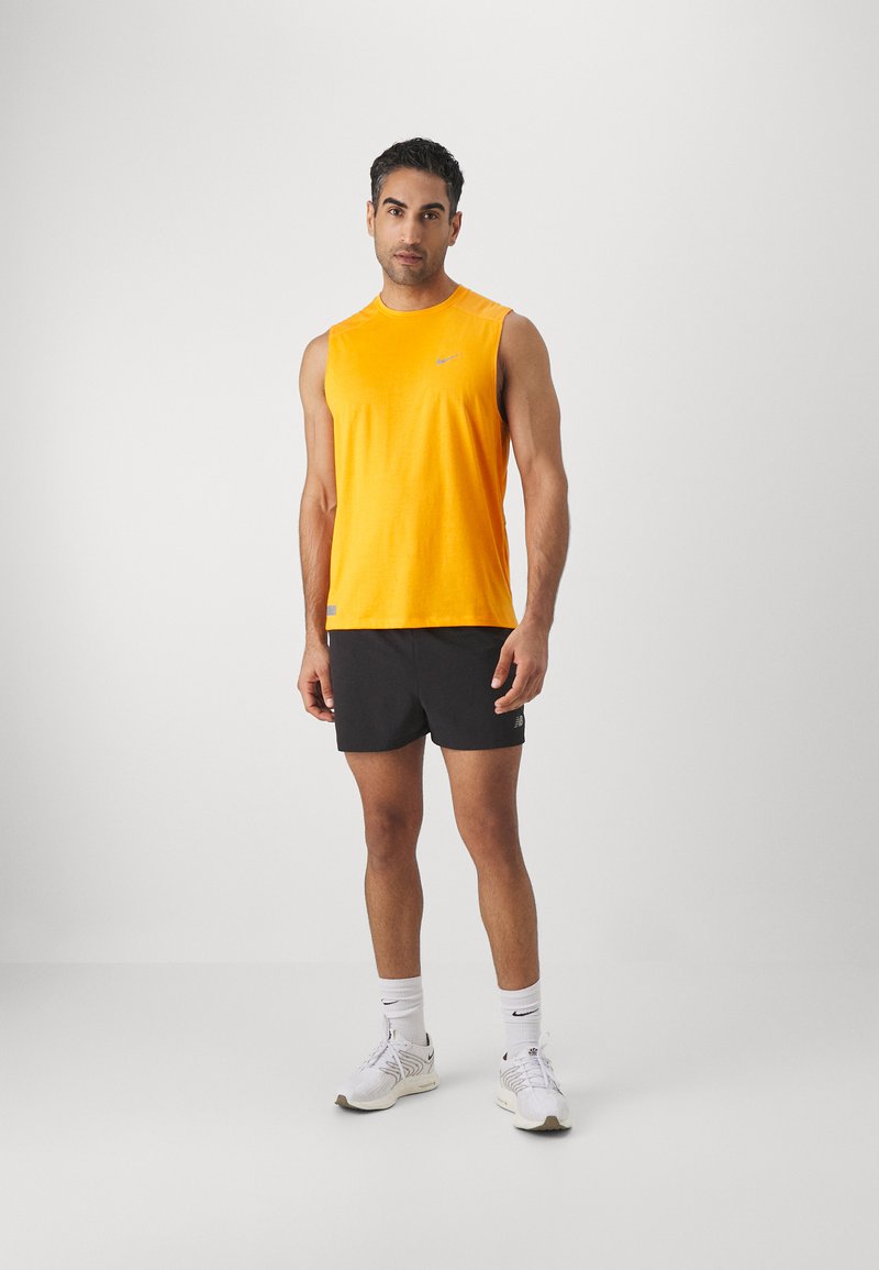 T-shirt de sport sans manches jaune en tissu léger, associé à un short noir. Baskets blanches avec des motifs subtils et des accents de logo.