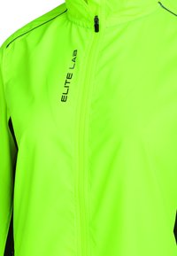 Neon-grüne Sportjacke mit einem Reißverschluss vorne, hohem Kragen und schwarzen Akzenten an den Seiten. "ELITE Lab"-Logo auf der linken Seite. Leichtes Material.